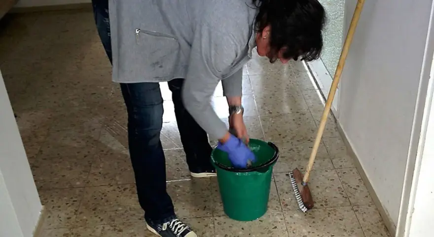 Sprzątaczka w szkole, w niebieskich rękawiczkach, przygotowuje się do pracy. Zastanawiasz się, ile zarabia sprzątaczka w szkole?