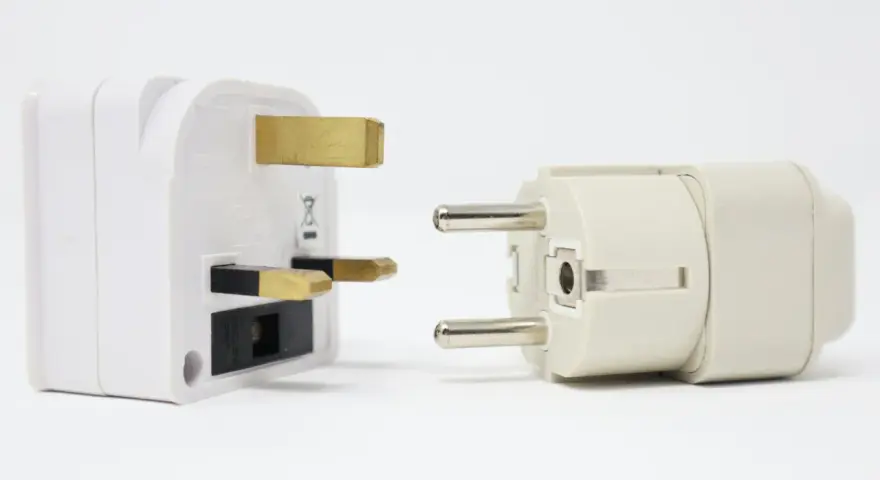 Adaptadores para diferentes tipos de enchufes: uno blanco con tres clavijas doradas y otro beige con dos clavijas plateadas.