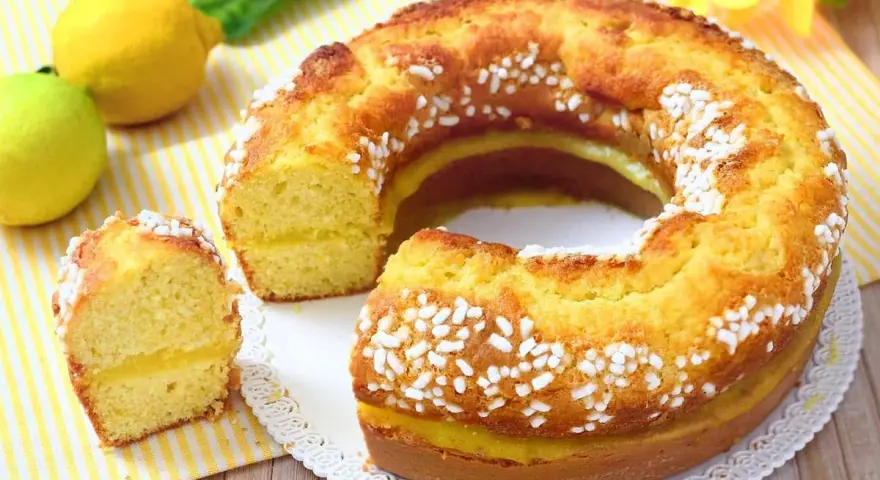 Un soffice ciambellone al limone, con una golosa crema gialla all'interno e decorato con perline di zucchero. Perfetto per la colazione o la merenda.