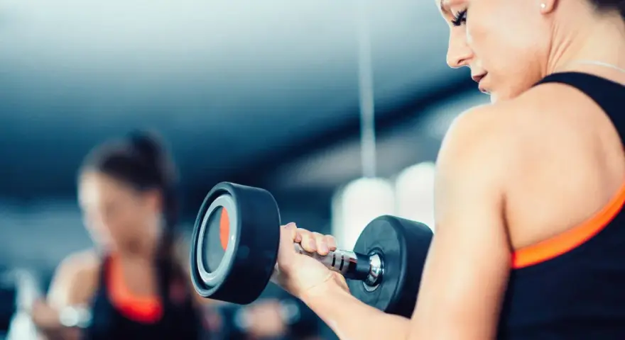 Frau hebt Hantel. Die Frage, wieviel kg darf eine Frau heben arbeitsrecht, ist hier nicht relevant, da es um Fitness geht.