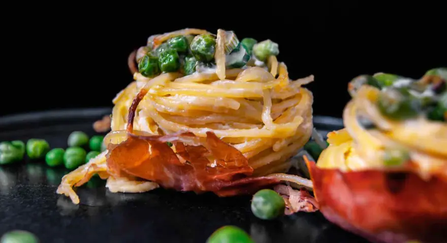 Köstliche italienische Pasta Vorspeisen mit Erbsen und Schinken, auf einem dunklen Teller angerichtet.