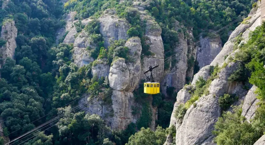 A bright yellow cable car ascends the rugged, tree-covered cliffs of Montserrat, Spain.