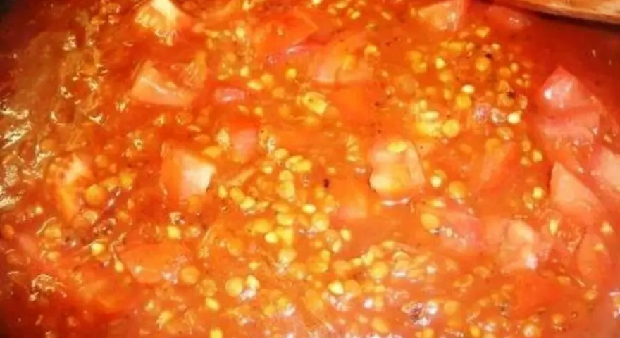 Buchweizen kochen mit Tomaten. Ein Holzlöffel rührt in der roten Sauce mit den Buchweizenkörnern und Tomatenstücken.