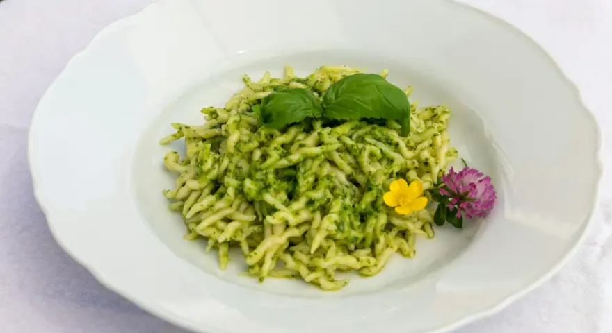 Pasta al pesto con hojas de albahaca fresca y flores comestibles.