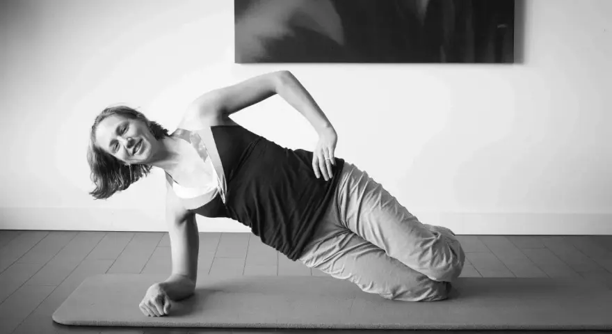 Femme souriante en plein gainage latéral sur un tapis de yoga.