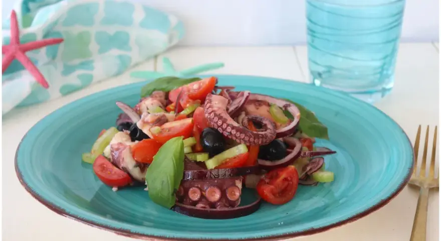 Un invitante polpo alla catalana su un piatto turchese, con pomodorini, olive e basilico. Fresco e saporito.