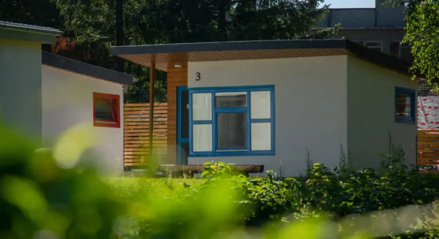 Nowoczesne domki letniskowe w osadzie Chmielaki. Jasne ściany, niebieskie okna i drewniane elementy tworzą przytulną atmosferę.