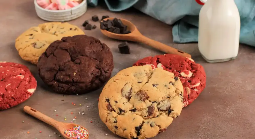 Verschiedene amerikanische Cookies: Schoko, Red Velvet und Chocolate Chip. Dazu Marshmallows, Schokostückchen und Milch.