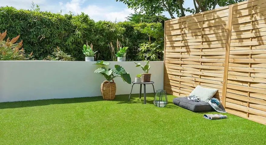 Terraza con césped artificial verde vibrante, plantas en macetas, un banco y una valla de madera.