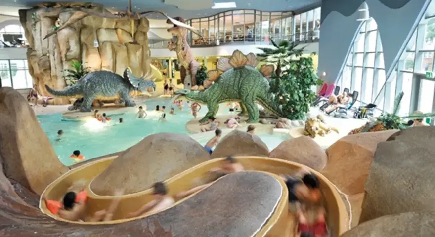 Kinder planschen im Dino-Bad, ein perfektes Ziel für die Herbstferien in Hamburg. Rutschen und Dinosaurier sorgen für Spaß.