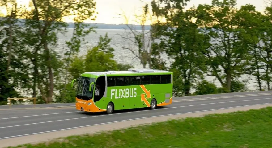 Zielony autobus Flixbus jedzie drogą przy jeziorze otoczonym drzewami.