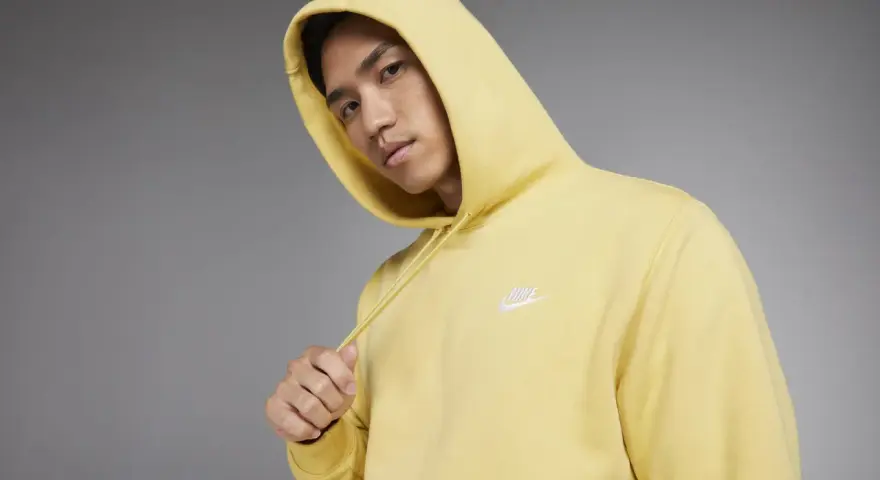 Młody mężczyzna w żółtej bluzie z kapturem Nike Club.