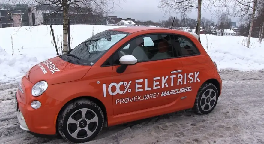 Pomarańczowy Fiat 500e w zimowej scenerii, z napisem "100% ELEKTRISK". Sprawdź zasięg tego elektryka!