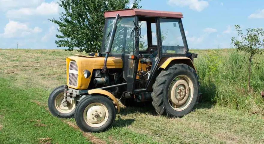 Żółty Ursus C-360 na łące. Pytanie o to, ile oleju do filtra powietrza C-360, jest kluczowe dla jego sprawnej pracy.