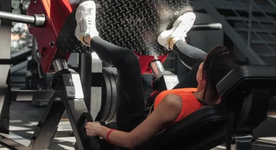 Kobieta ćwiczy na maszynie do wyciskania nóg, wykonując ćwiczenie push pull legs.