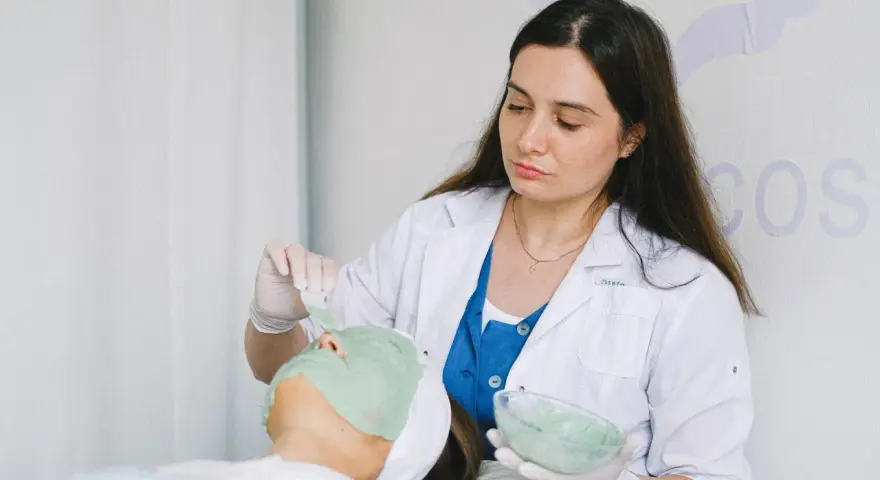 Dermatolog nakłada zieloną maskę na twarz pacjentki.