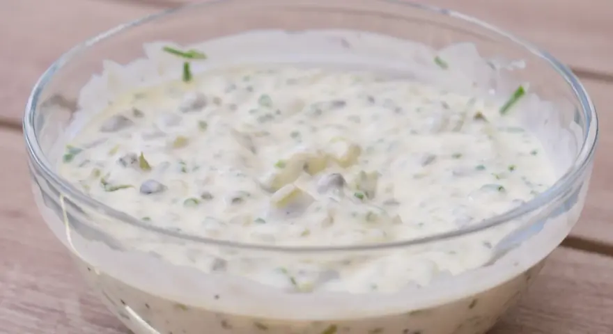 En krämig kall sås till fisk, med kapris och örter, serverad i en glasskål på en träyta.