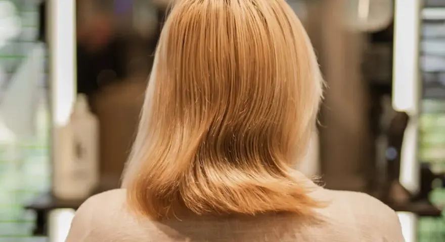 Kobieta z blond włosami, zastanawia się, jak nosić siwe włosy. Włosy są średniej długości, lekko falowane.
