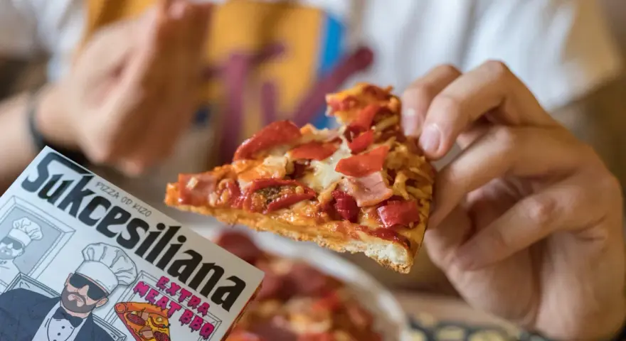 Kawałek pysznej pizzy od Kizo, z dodatkami mięsnymi i papryką, na opakowaniu widnieje napis "Sukcesiliana Extra Meat BBQ".
