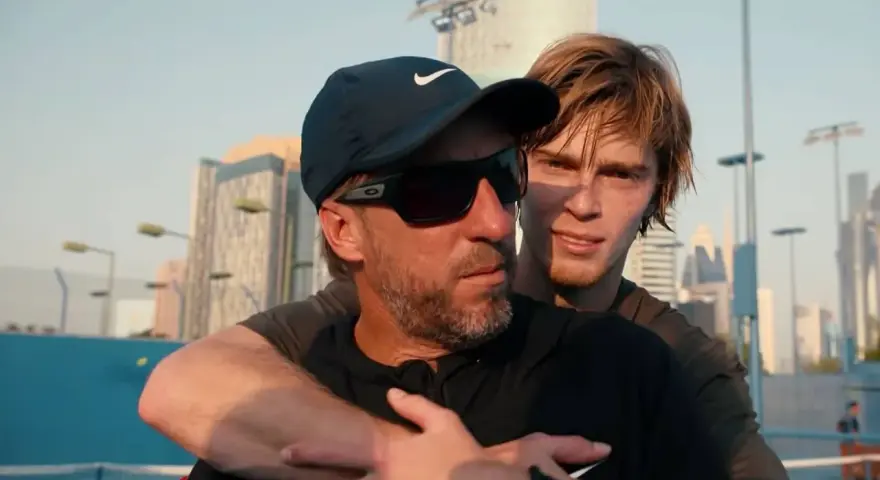 Fernando Vicente, entrenador de tenis, abraza a su pupilo en una cancha con rascacielos de fondo.