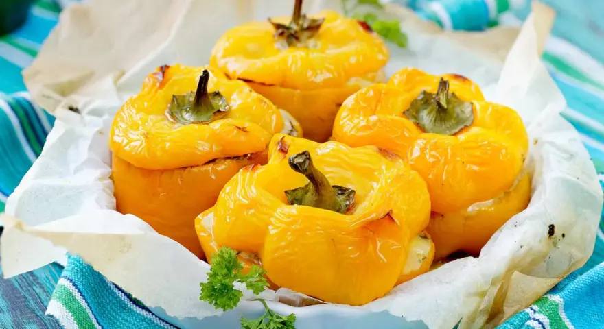 Quatre poivrons farcis jaunes, dorés et appétissants, servis dans un plat garni de papier sulfurisé et décorés de persil frais.