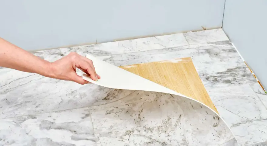 Mano retirando capa de vinilo del suelo. Un paso clave para saber como quitar pintura de caucho del suelo.