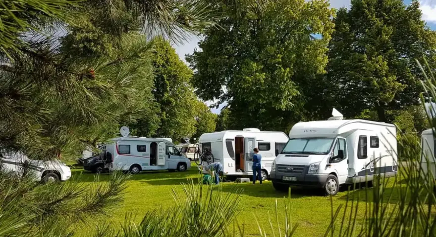 Kilka kamperów zaparkowanych na zielonym trawniku, w otoczeniu drzew. Idealne miejsce na wakacje w kamper park.
