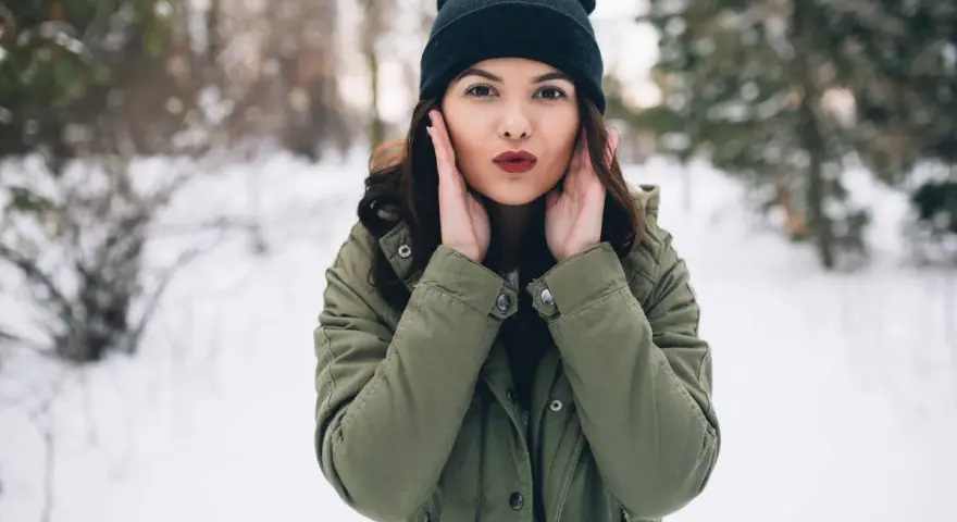 Zastanawiasz się, jaki szalik do zielonej kurtki? Ta dziewczyna w zimowym lesie ma czarną czapkę i zieloną kurtkę.