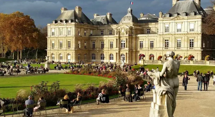 Palacio de Luxemburgo y su jardín con gente sentada y un monumento.