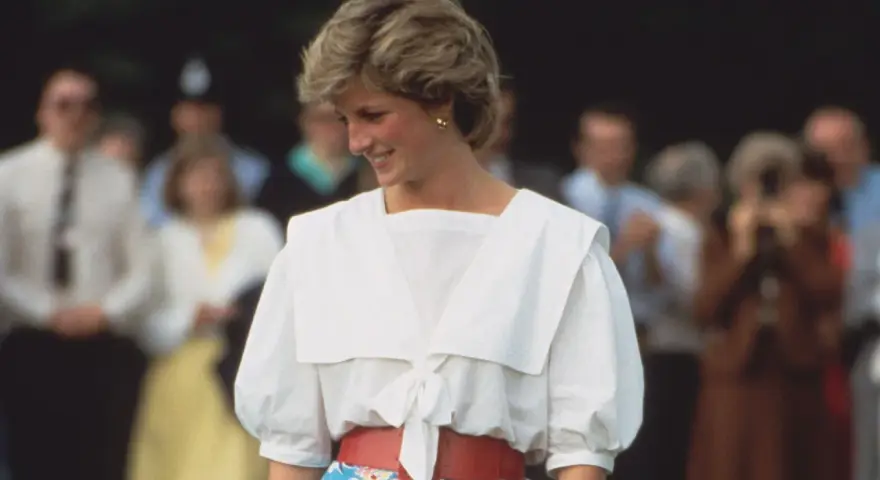 Lady Di sonríe con un conjunto blanco y rojo, un ejemplo de sus icónicos outfits.
