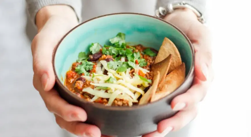 Miseczka pysznego chili con carne przepis, posypana serem i świeżą kolendrą, z chrupiącymi nachos. Idealne na chłodne dni.