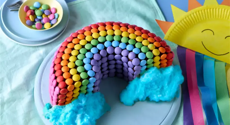 Bunter regenbogen kuchen, verziert mit vielen bunten Smarties und blauer Zuckerwatte als Wolken. Ein Fest für die Augen!
