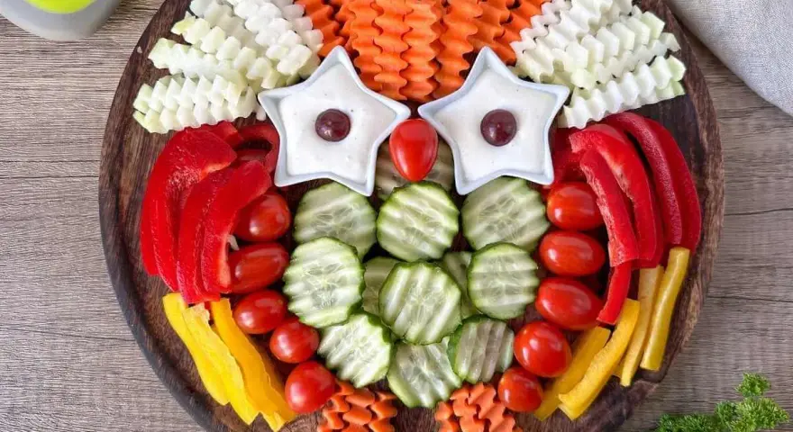 Eine bunte Rohkostplatte für Kinder, gestaltet als lustige Eule mit Sternen als Augen und verschiedenen Gemüsesorten.