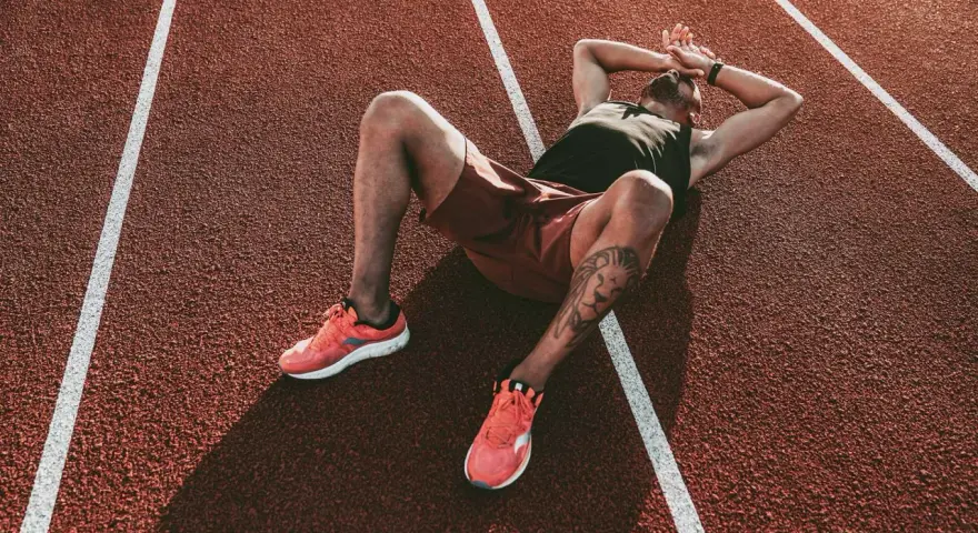 Atleta esausto sdraiato su una pista da corsa, con le mani sulla testa, forse vittima della sindrome da overtraining.