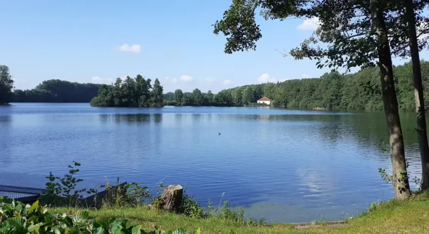 Ein ruhiger Lippstadt See mit bewaldeten Ufern und einem kleinen Haus am Horizont.
