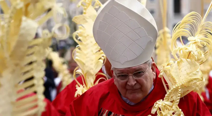 A bishop in red vestments and a white mitre holds a palm frond, surrounded by others. This scene marks Passion Sunday.