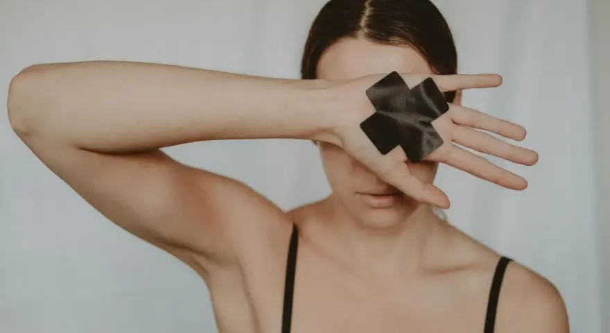 Kobieta zakrywa oczy dłonią z czarną taśmą w kształcie krzyża, symbolizującą trauma seksualna i potrzebę uzdrowienia.