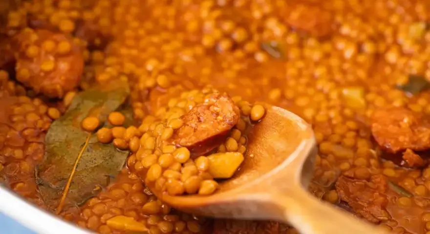 Primer plano de lentejas con chorizo y laurel en una cuchara de madera.