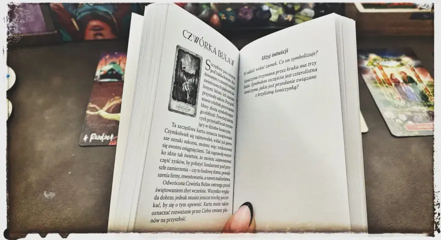 Mistycyzm i tarot marzyciela: otwarta księga z kartą "Czwórka Buław" i innymi kartami tarota.