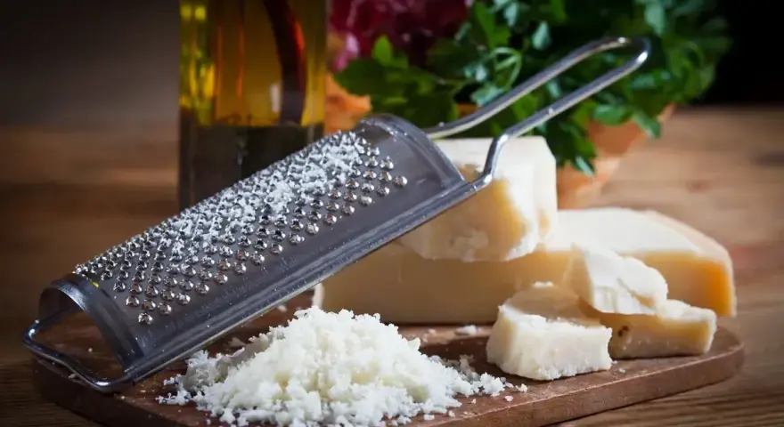 Tarka z kawałkami sera **padano ser** i świeżo startym serem. Obok butelka oliwy i zielenina.