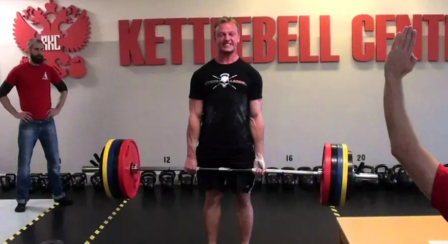 Man i gymmet förbereder sig för ett styrkelyft program. Han håller i en skivstång med vikter.