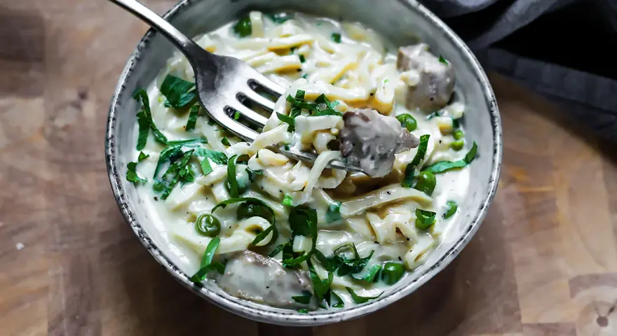 Keto makaron w kremowym sosie z groszkiem i mięsem, nabierany widelcem.