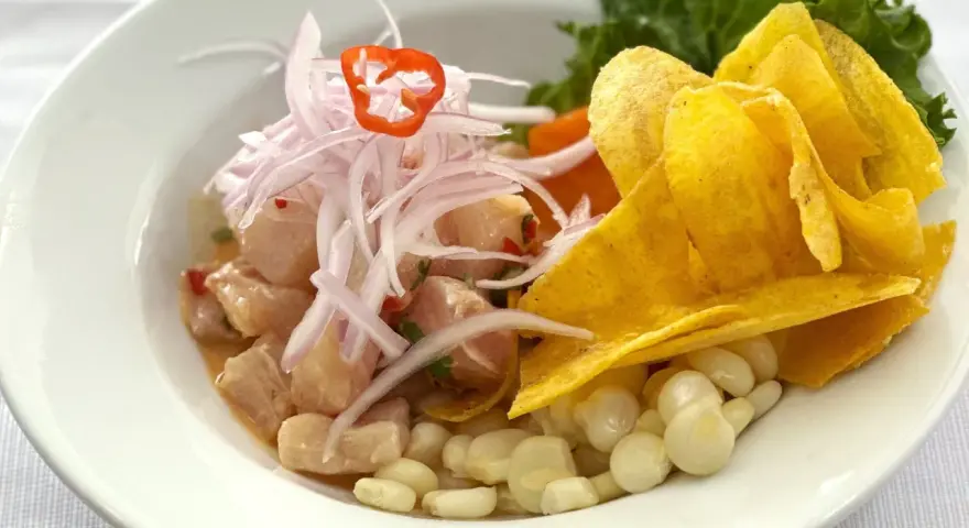 Delicioso ceviche peruano con trozos de pescado fresco, cebolla morada, chile, maíz tierno y chips de plátano.