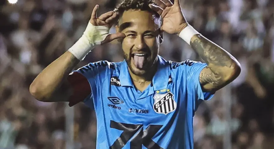 Neymar w niebieskiej koszulce Santos z charakterystycznym gestem i wystawionym językiem. Tak wygląda boisko, gdzie gra Neymar.