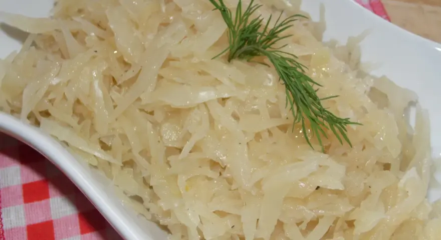 Gotowana biała kapusta do obiadu, podana w białej misce, ozdobiona gałązką koperku.