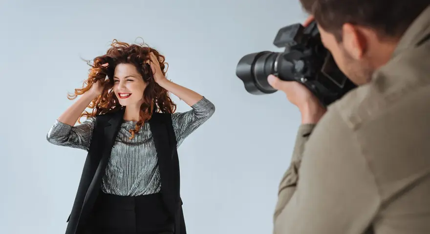 Modelka z burzą rudych włosów pozuje do zdjęcia. Fotograf robi jej zdjęcie. To sesja TFP, co to znaczy?