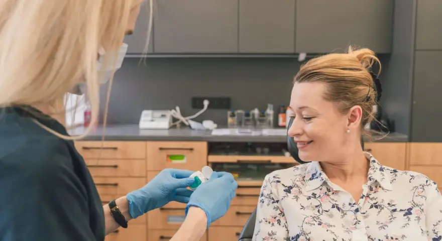 Dentystka w rękawiczkach przygotowuje preparat do fluoryzacji w ciąży. Uśmiechnięta pacjentka czeka na zabieg.