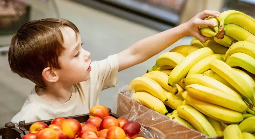 Chłopiec sięga po banana. Co zrobić, gdy dziecko kradnie w sklepie? Rozmowa i nauka uczciwości to klucz.