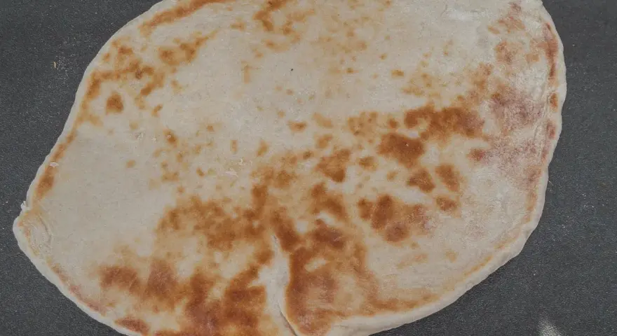 Un naan au fromage, peut-être avec un peu de La Vache qui rit, doré et moelleux, prêt à être dégusté.