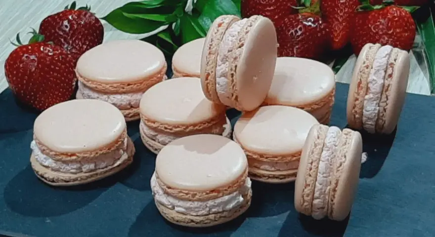 Delikatne makaroniki na mące migdałowej lub kokosowej, z kremowym nadzieniem i świeżymi truskawkami w tle.